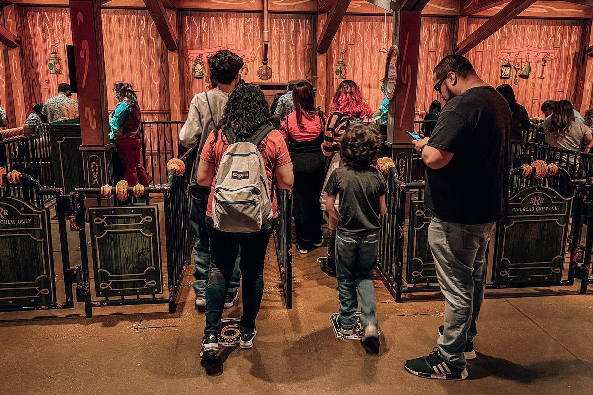 A family seen from behind standing in line at an old-west themed ride at Disneyland; one of the women is wearing a backpack. 