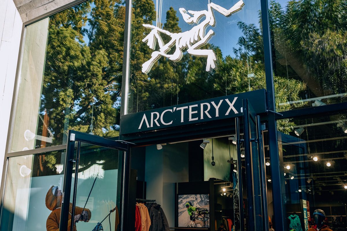 A glass front entrance to an Arc'teryx store with trees showing the reflection.