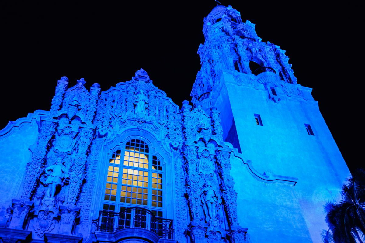 A night time view looking upwards at an ornate Spanish-style building illuminated with blue light.