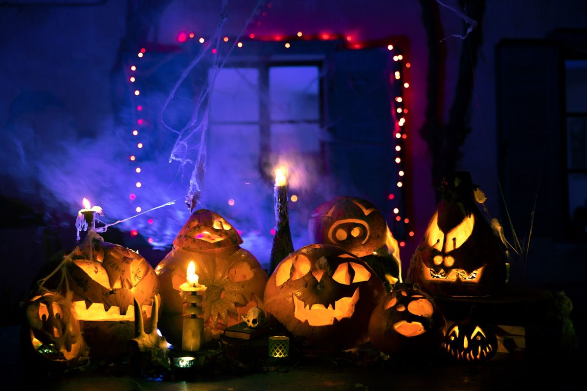 A display of glowing carved pumpkins amidst candles with a dimly lit, purple smokey backdrop.