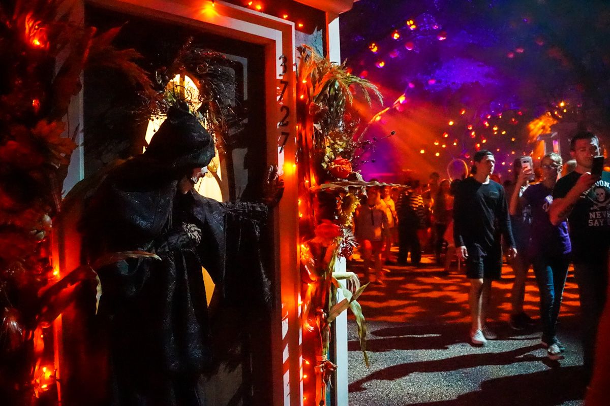 A crowd of people walking through a haunted house attarction lit by orange and purple lights, with a grim reaper display in the foreground.