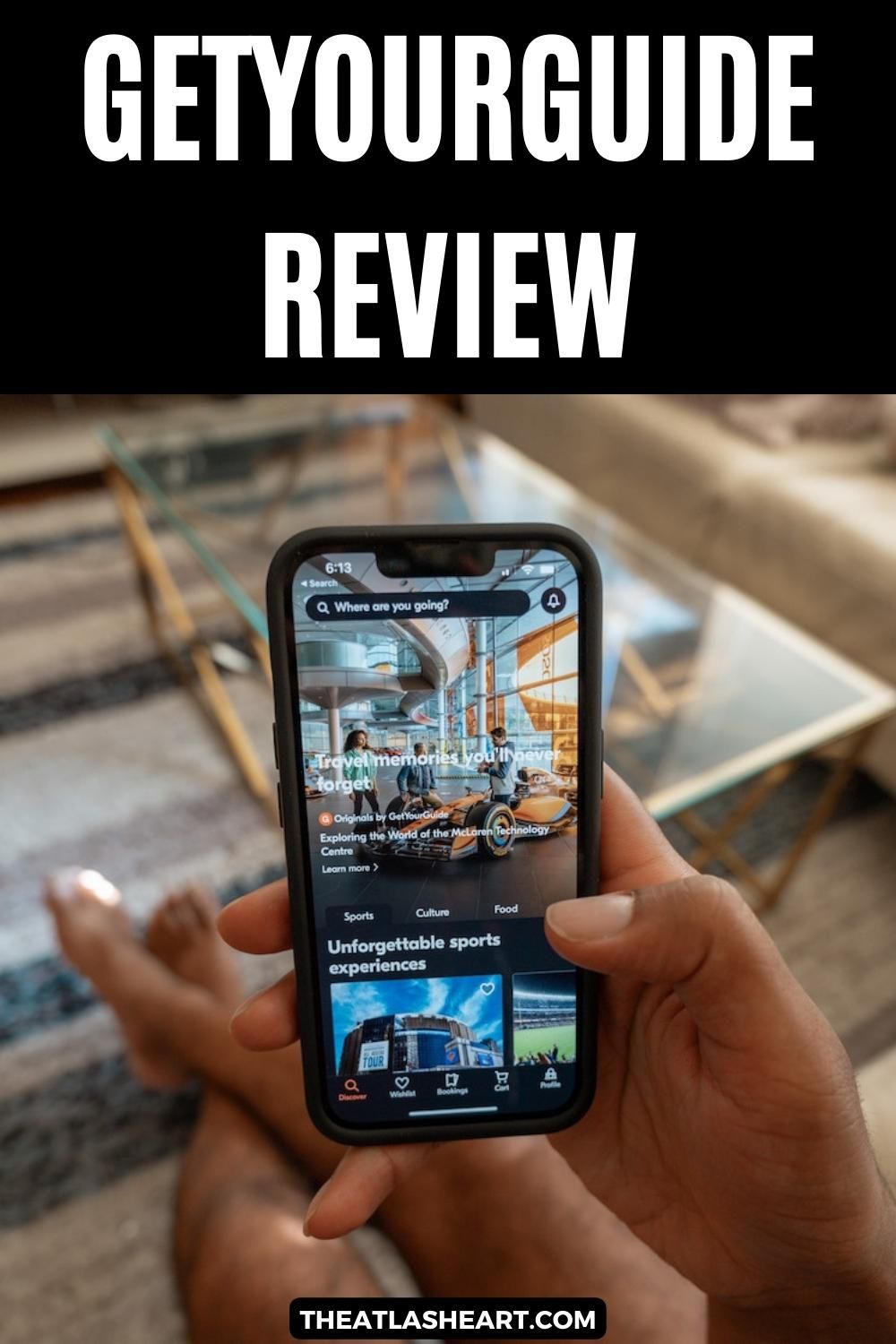A hand holds an iPhone, looking at the GetYourGuide app, with a soft-focus living room in the background, with the text overlay, "GetYourGuide Review."