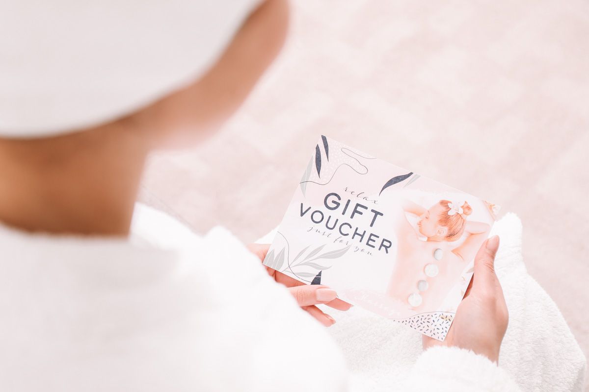 Looking over the shoulder of a woman wearing a white bathrobe, looking down at a spa gift voucher in her hands.
