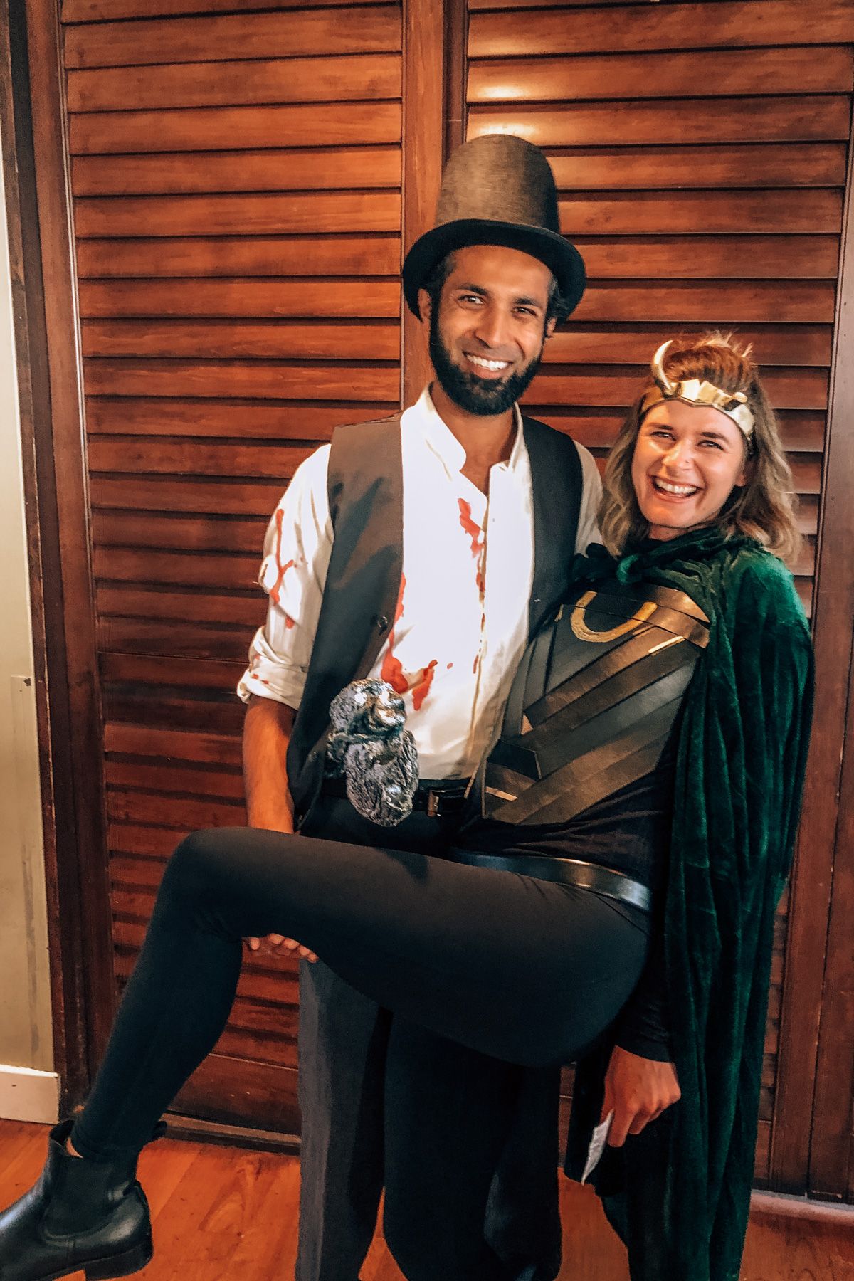 A happy couple in Halloween Costumes poses in front of a wooden closet door, getting ready to attend Halloween Events in San Francisco.