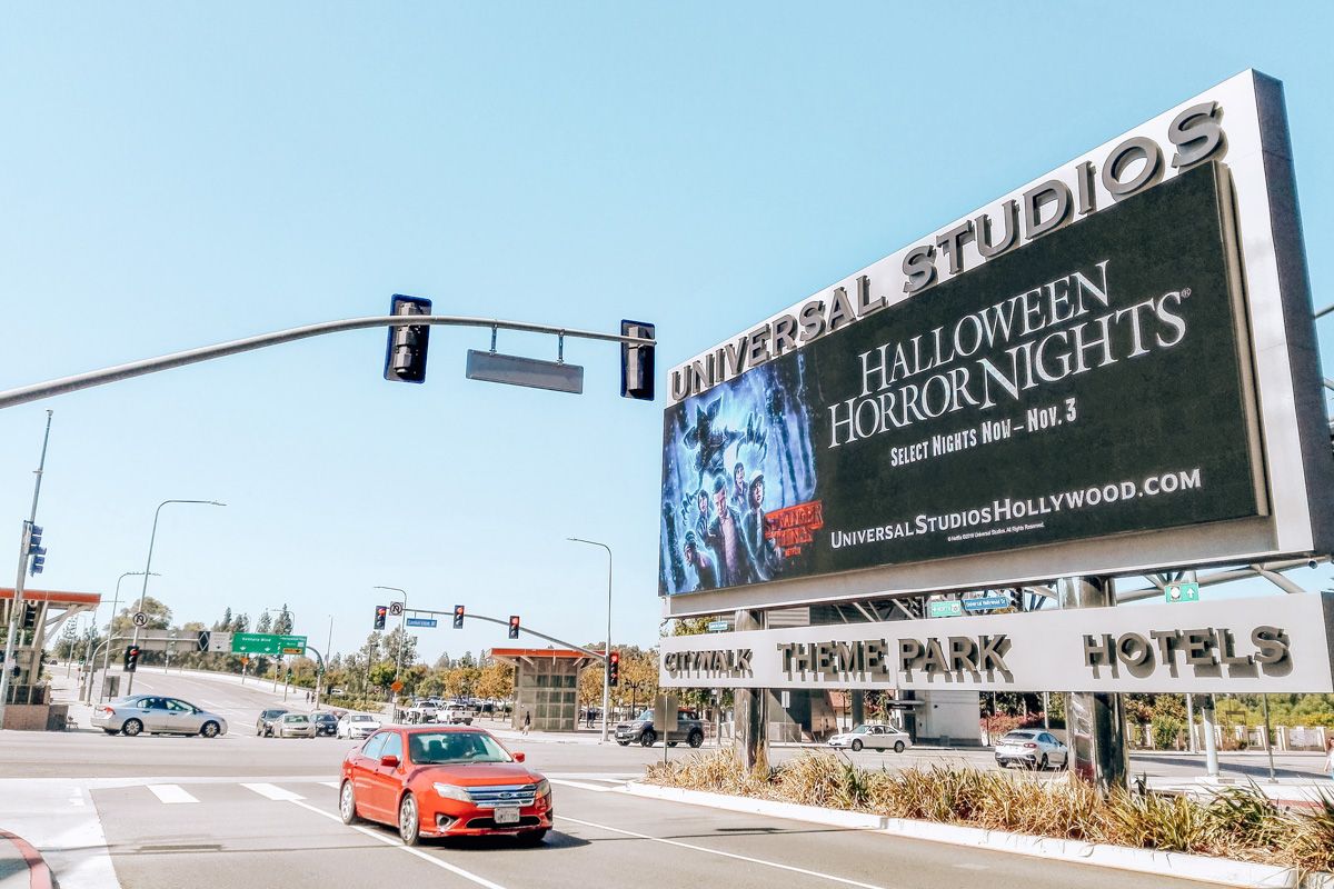 A billboard advertising Halloween Horror Nights at Universal Studios alongside a wide, suburban road on a clear, sunny day.
