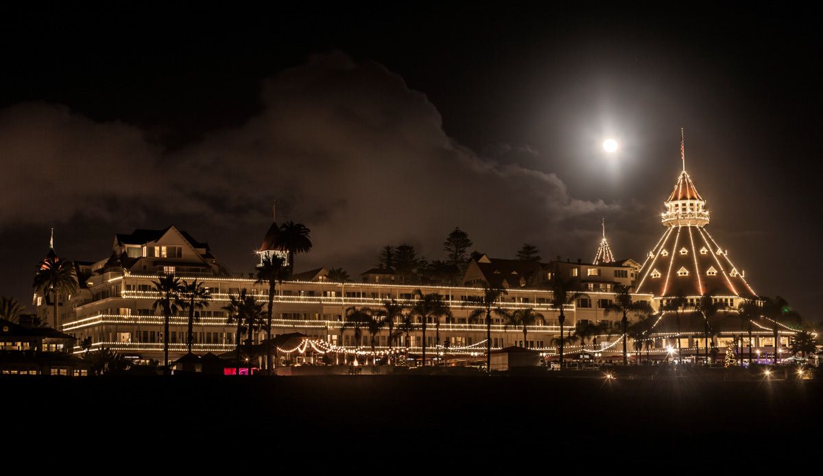 The Hotel del Coronado seen at night lit with white Christmas and surrounded by by silhouettes of palm trees.