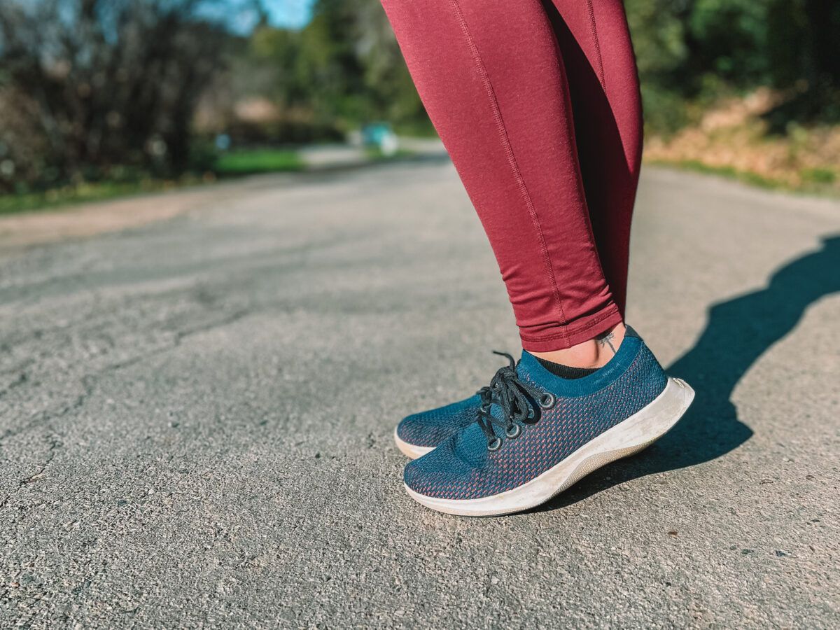 A close up of the Allbirds Dashers shoes as a woman in merlot leggings poses while out for a walk in California.