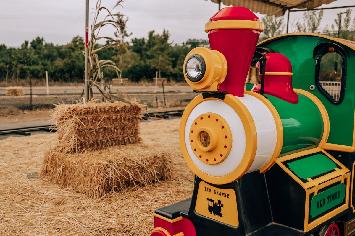 A red, white, yellow and green children's replica of a steam engine train, with straw and hay bales stacked in the background at Rancho Bernardo Pumpkin Station.