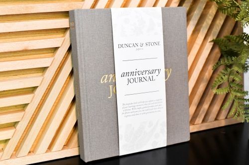 Product image for the grey Anniversary Journal, pictured leaning against a blond wood wall. 