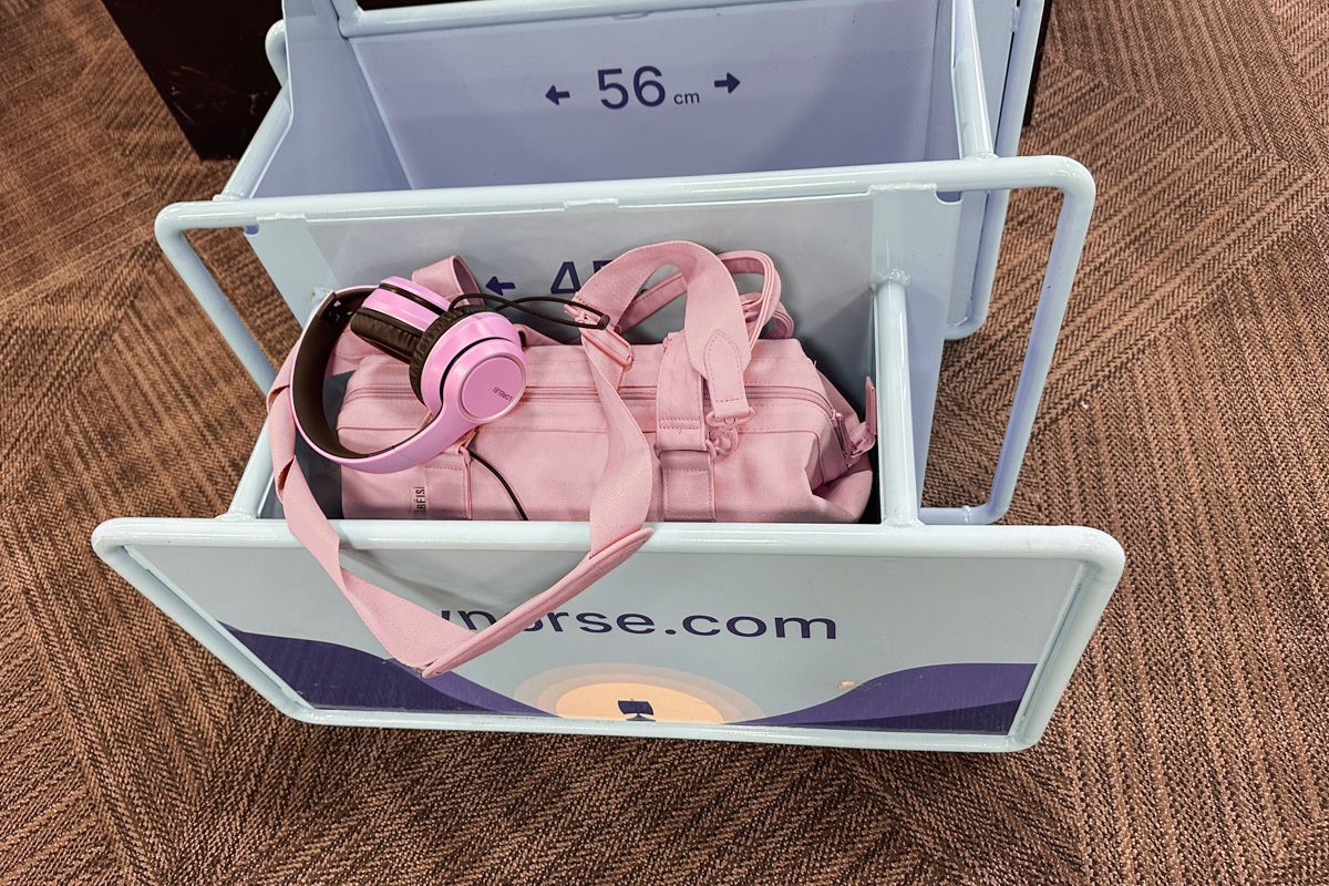 A pink Béis Mini Weekender Bag sitting inside a Norse Airlines baggage size bin with a pair of lavender headphones sitting on top.