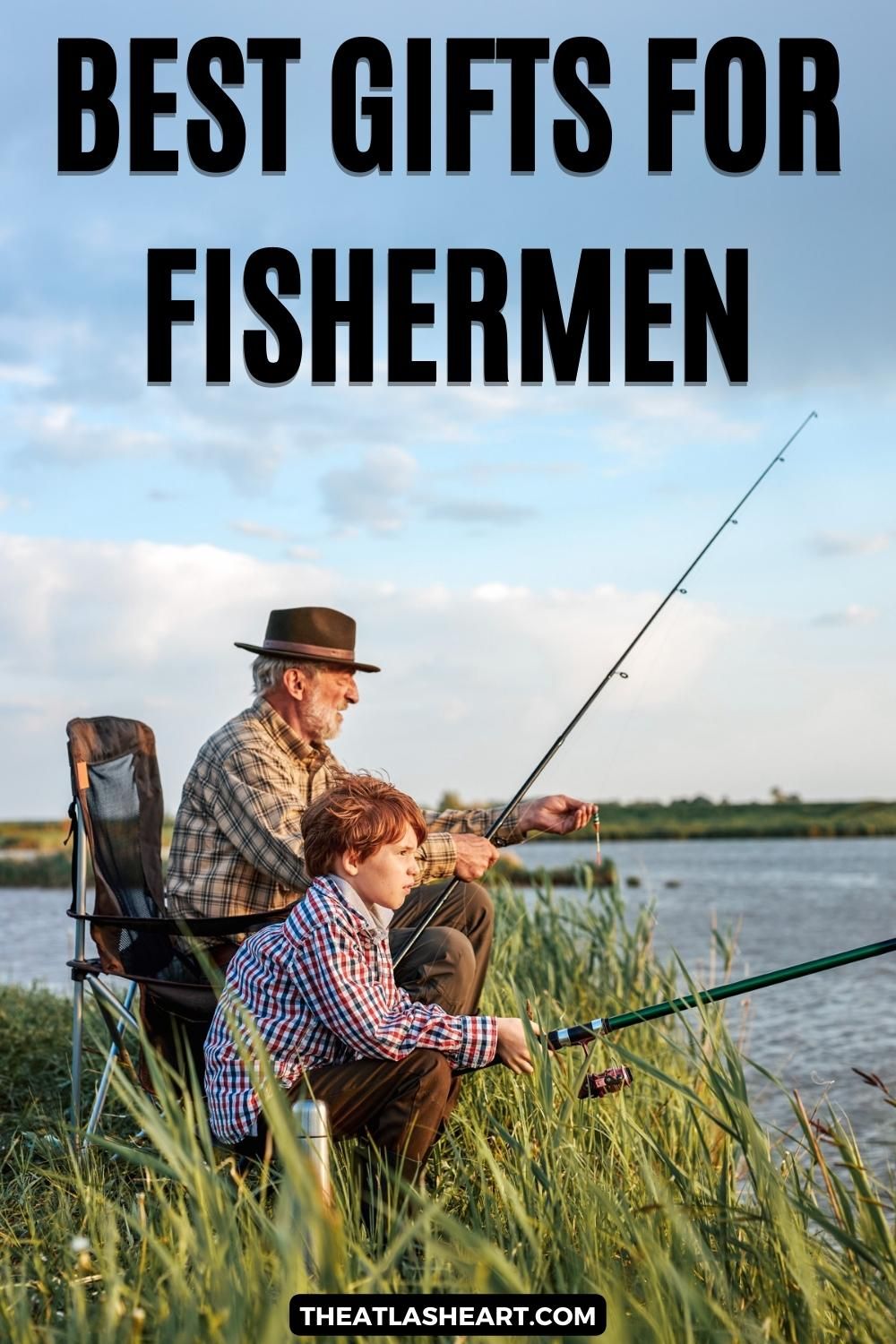 An older man in a brown, brimmed hat holding a fishing pole sits in a chair in tall grass on the banks of a lake with a young, red-haired boy in a checkered shirt sitting beside him holding a fishing pole, "Best Gifts for Fishermen."