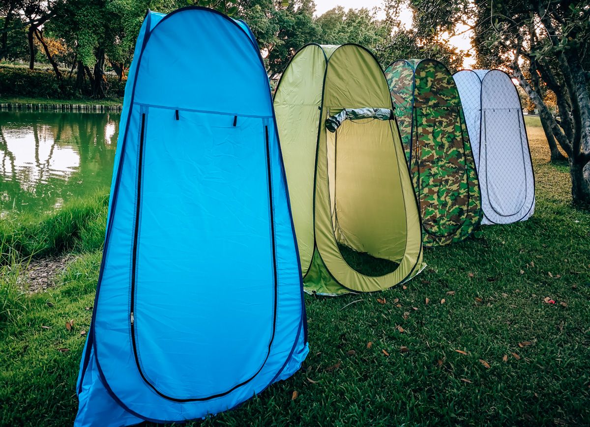 Buying Guide: How to Choose the Best Shower Tent
Four different colored shower tents in a line, blue, green, camo, and white, next to a river.