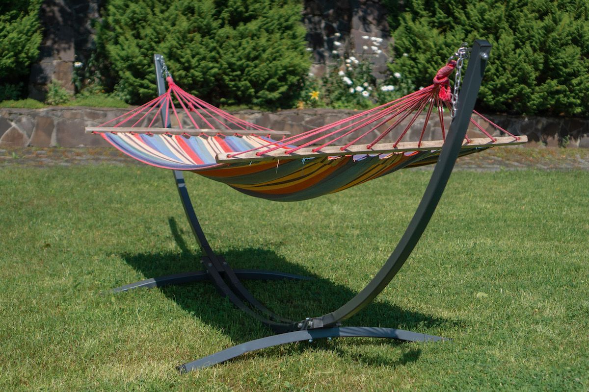 A rainbow-striped hammock on a freestanding hammock stand on a lawn in a backyard setting.