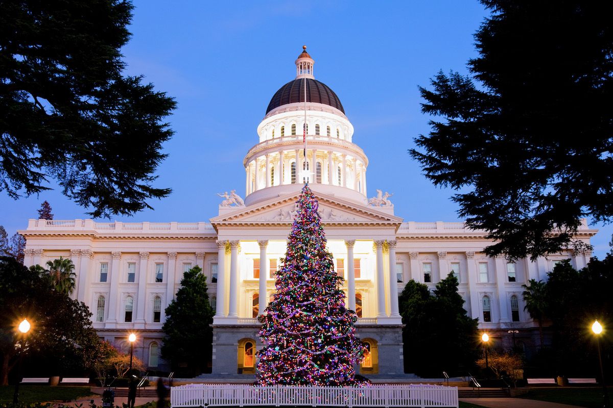 A view of the Capitol Building in the early evening during Christmas in Sacramento, with an illuminated Christmas tree in the foreground.