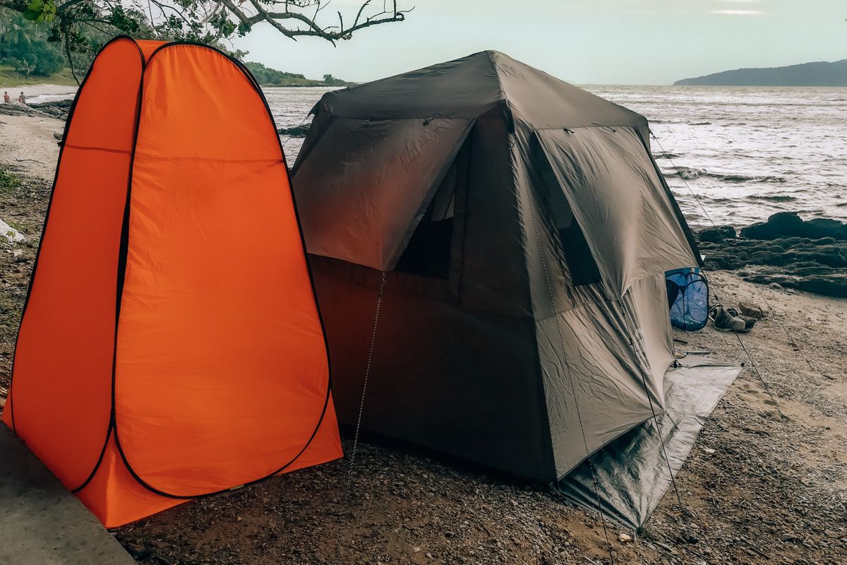 Conclusion: What is the Best Shower Tent?
An orange shower tent standing beside a grey damping tent, in front of a body of water.