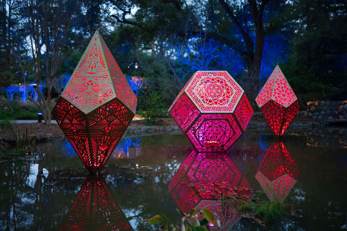 Enchanted, Descanto Gardens
Three geometric installations glow pink and appear to float over a pond, as blue lights illuminate trees in the distant background.