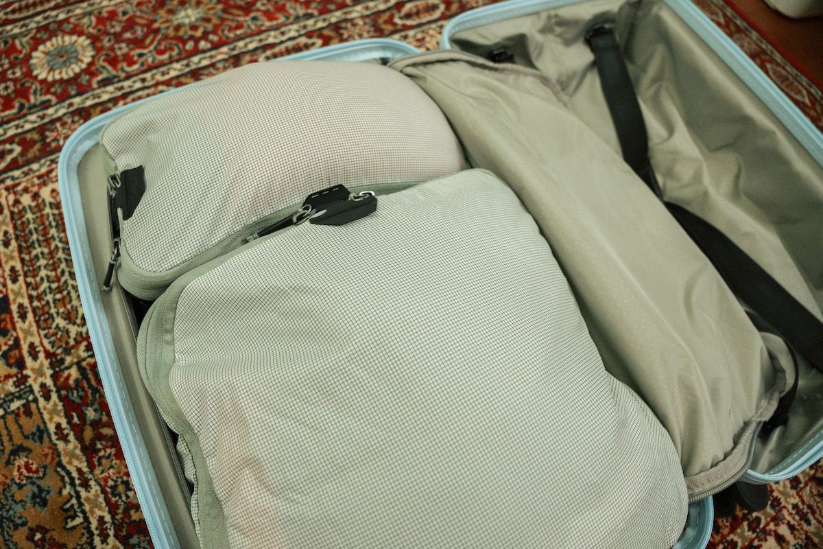 An open suitcase filled with packing cubes sitting on a red oriental rug on the floor.