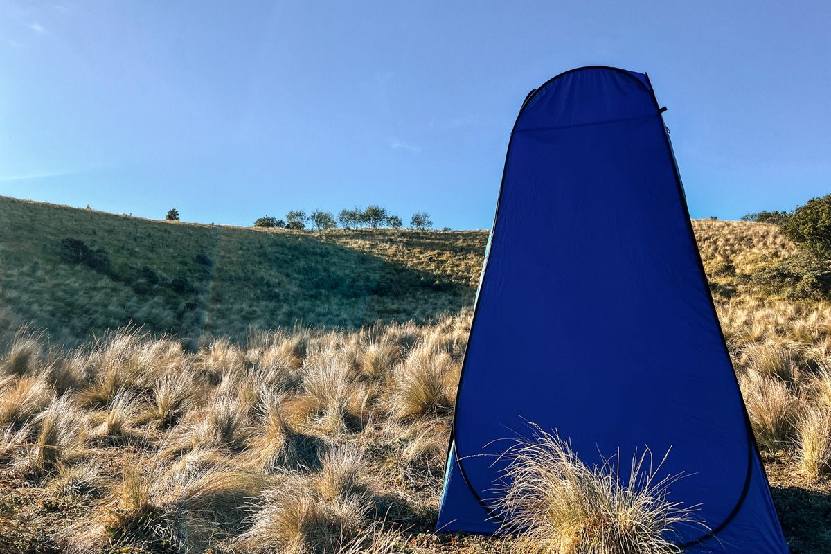 FAQs About Shower Tents 
A dark blue shower tent standing in a dry field with tufts of dry grass.