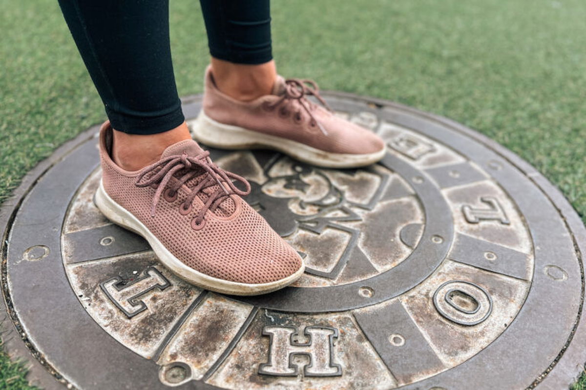 A pair of feet wearing some of the best travel shoes for women, Allbirds Tree Breezers, standing on a Mickey Mouse manhole cover surrounded by astroturf.