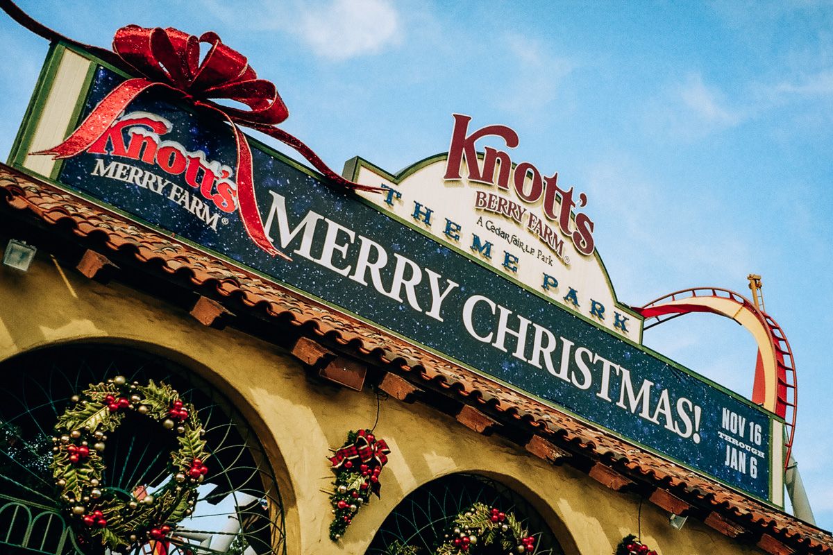Knott’s Merry Farm, Buena Park
The entrance sign reading, "Merry Christmas!", decorated with a giant red bow and positioned over yellow arches of Knott's Merry Farm entrance, with a blue sky in the background.