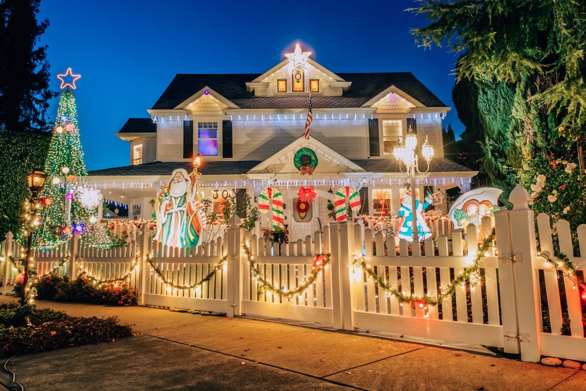 A suburban Bay Area house lit up with Christmas decorations, seen at dusk form the sidewalk.