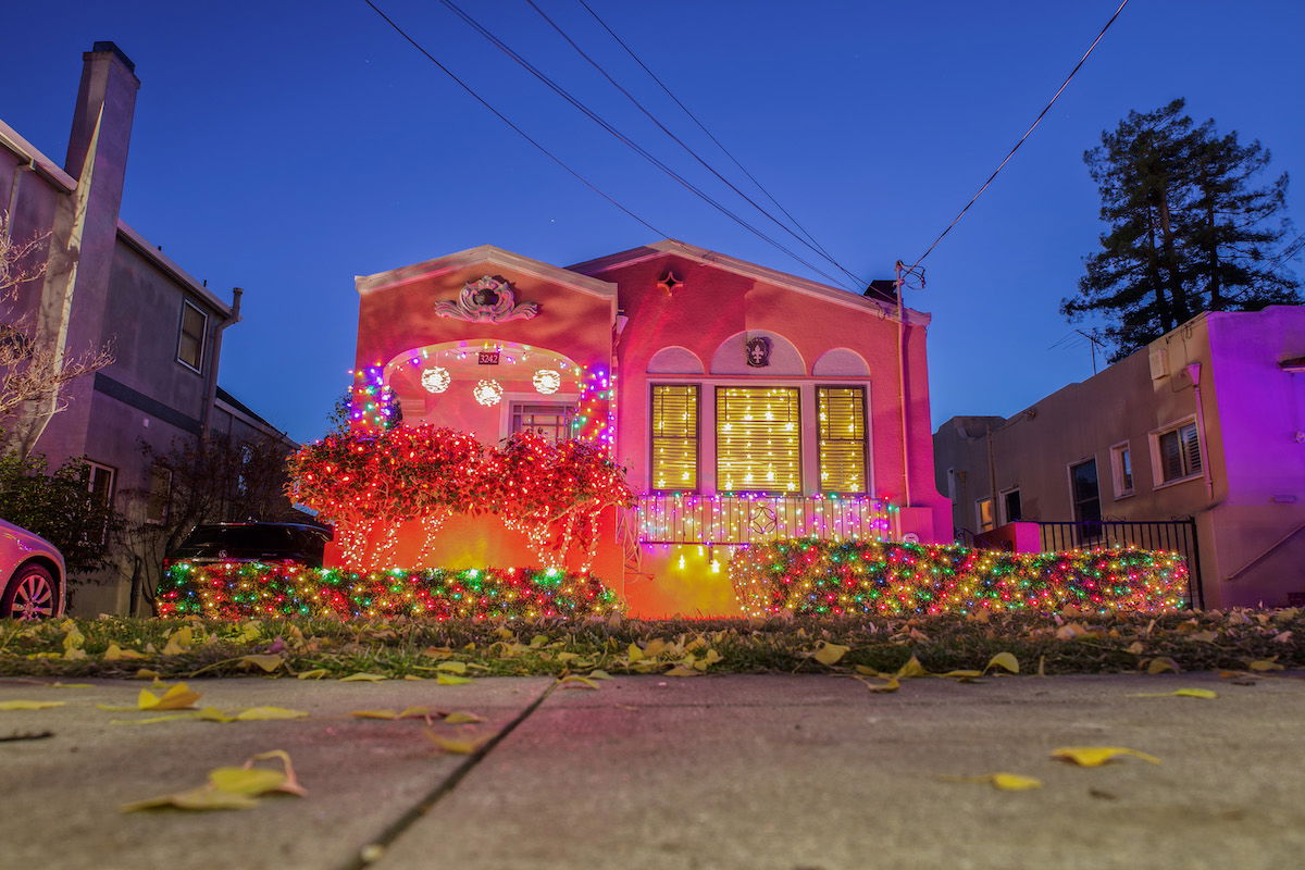 A Bay Area Spanish-style stucco house glowing pink and decked out in Christmas lights just after dusk. 
