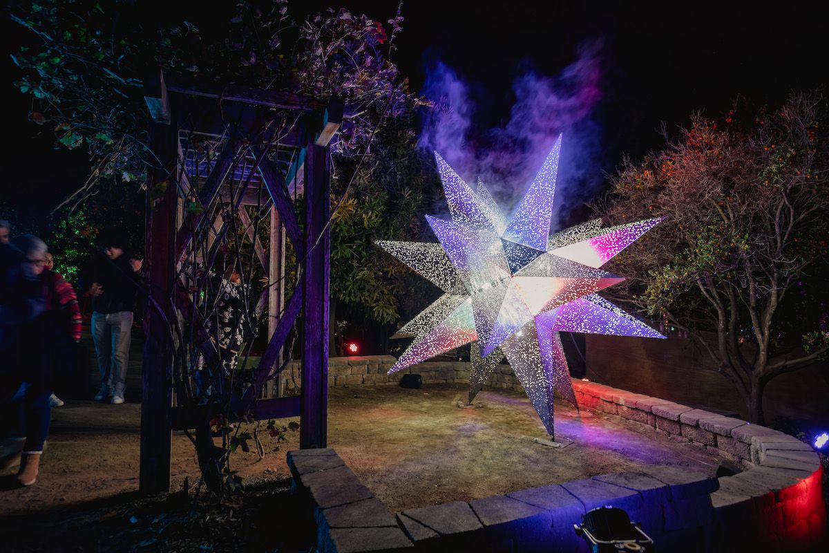 A nighttime scene of a star-shaped sculpture illuminated with purple light at the San Diego Botanical Garden Lightscape.