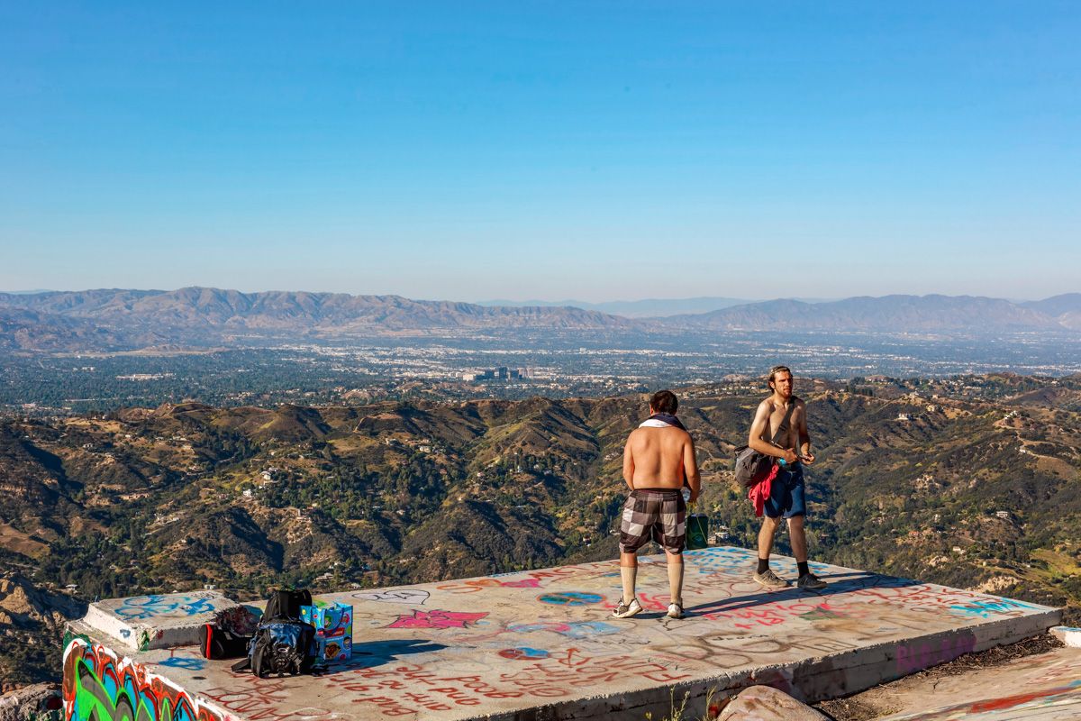 Top Of Topanga Overlook
Two shirtless men dancing on a cement platform that's covered in graffiti and offers a clear view of the city and mountain ridge in the back.