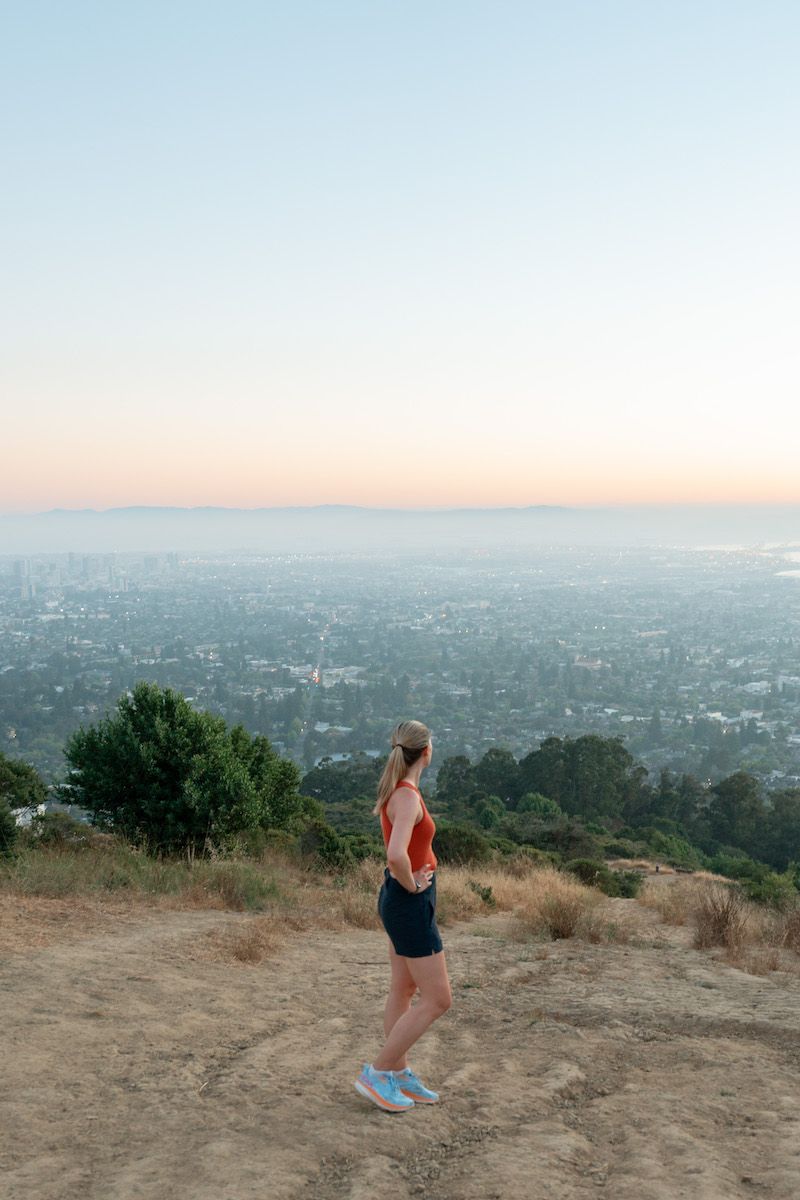 Mimi looking at the skyline from a hiking lookout point above Berkeley, California while she wears her best Hoka running shoes.