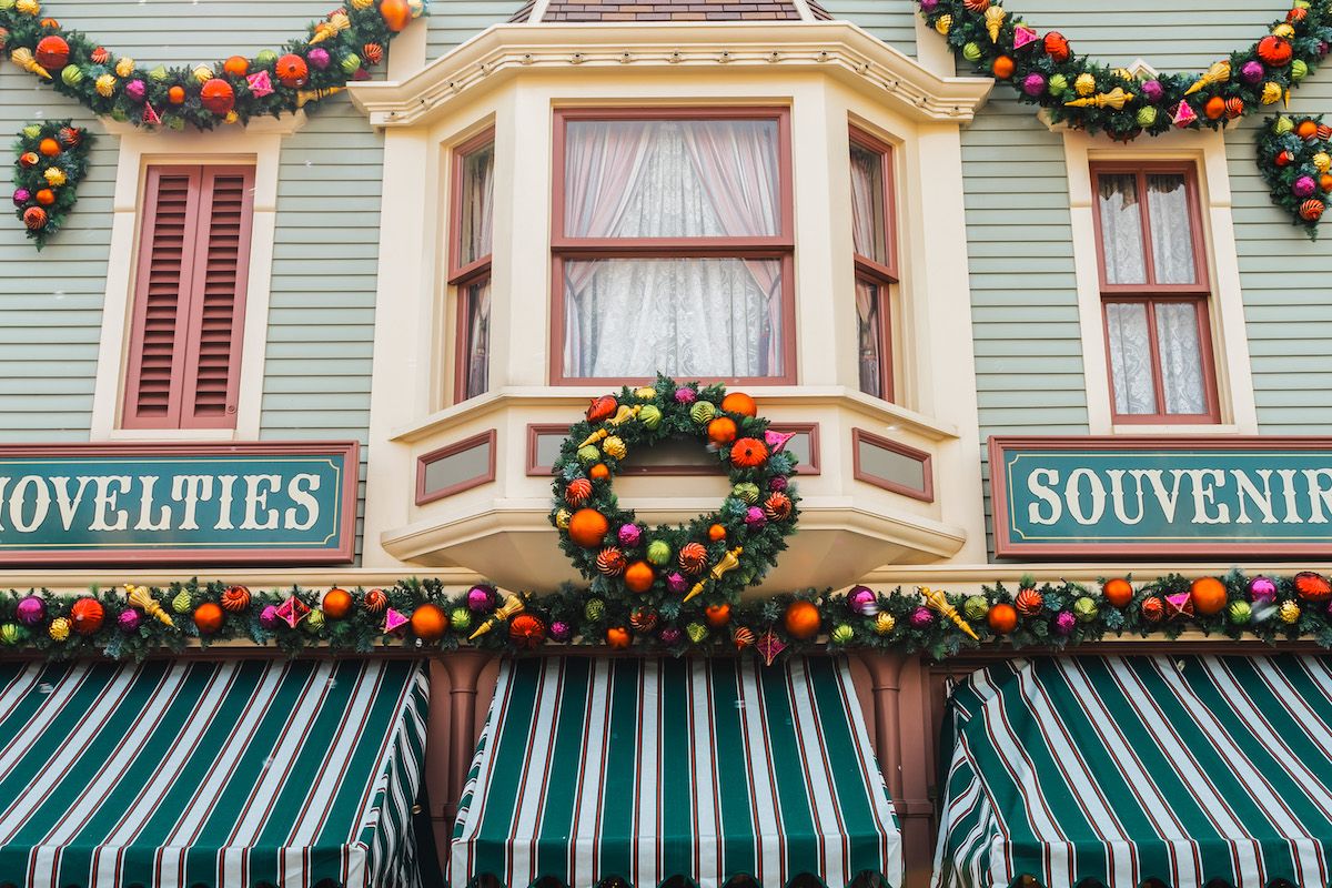 The facade of a light green Victorian building decorated with Christmas wreaths and garlands, with white and green striped awnings.
