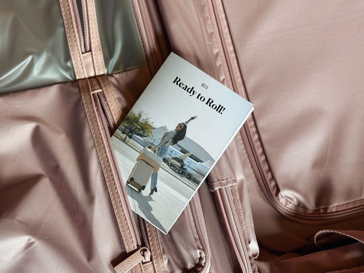 A close-up of the pink interior of a Beis Suitcase with a small Beis pamphlet sticking out of the pocket the phrase, "Ready to Roll!" printed on the cover.