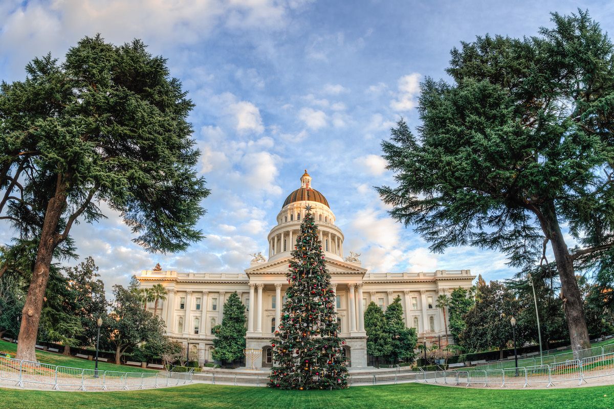 A view of the Capitol Building during Christmas in Sacramento, with a Christmas tree in the foreground and a partly-cloudy sky in the background.