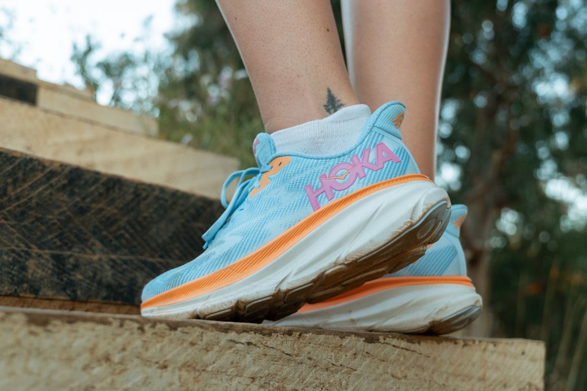 Close-up of a pair of feet wearing light blue Hoka walking shoes while climbing a set of outdoor steps.