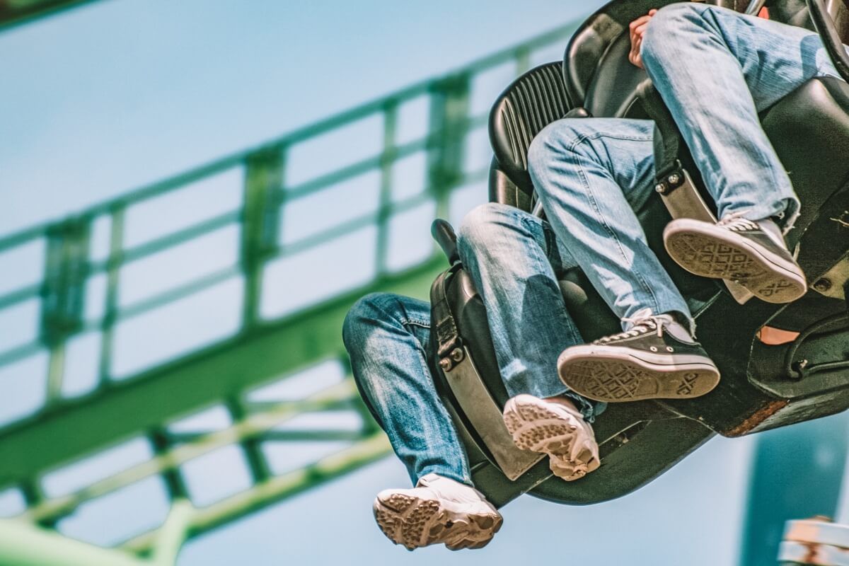 Two pairs of feet dangling from green roller coaster seats with a clear blue sky in the background.