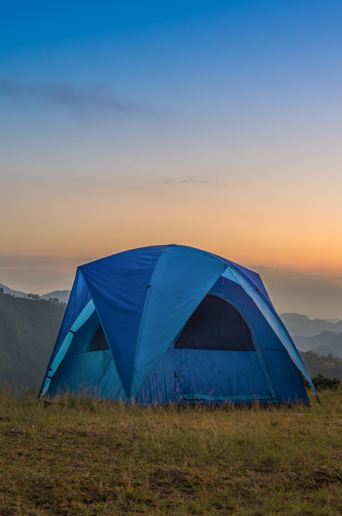 Best Tall Tents
A blue tent standing tall on a grassy hill with a sunset or sunrise silhouetting the mountain ranges in the background.
