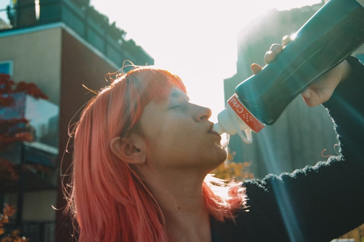 The author of this cirkul water bottle review, a pink-hair woman seen in profile with her head tipped back as she sips from a Cirkul bottle.