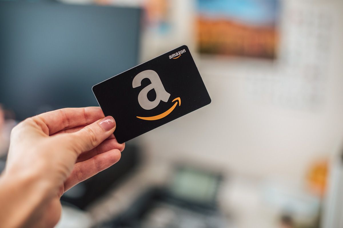 A hand holding an Amazon gift card against a soft-focus backgound.