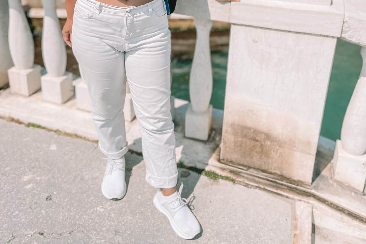 A woman white jeans and white Vessi shoes seen from the waist down stands on a bridge in Venice.