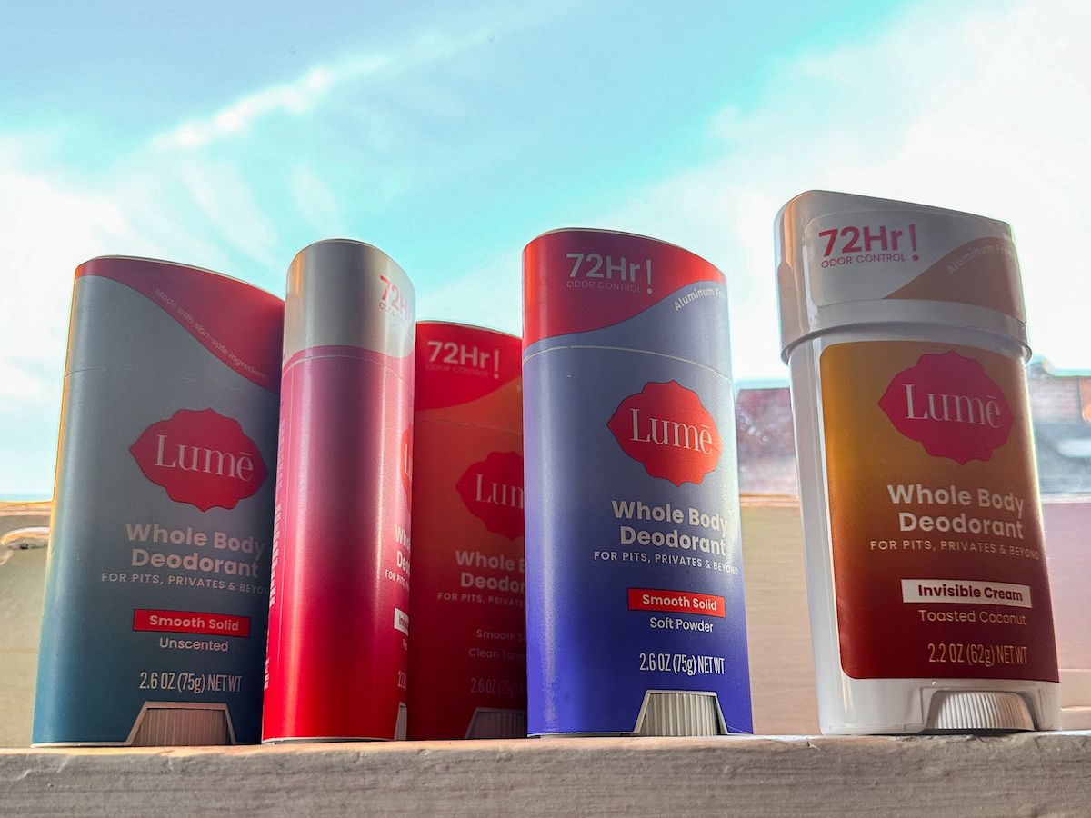 Several sticks of Lume deodorant lined up on a windowsill, with a blue sky visible through the windowpane.