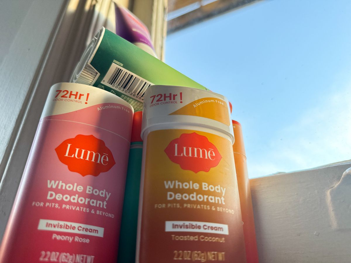 A stack of Lume deodorants in various scents, seen from below 
while stacked on a windowsill, with a blue sky visible through the pane.