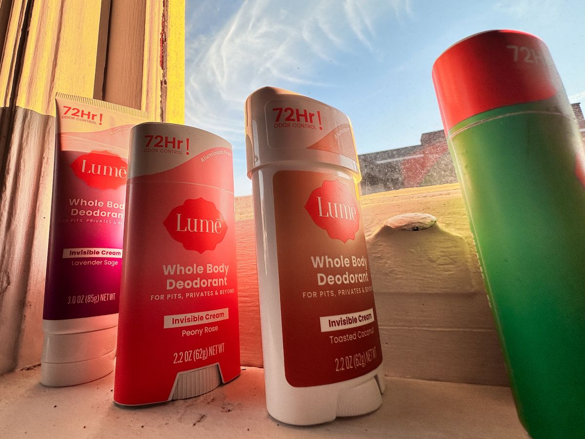 Several sticks of Lume deodorant lined up on a windowsill, with a blue sky visible through the windowpane.