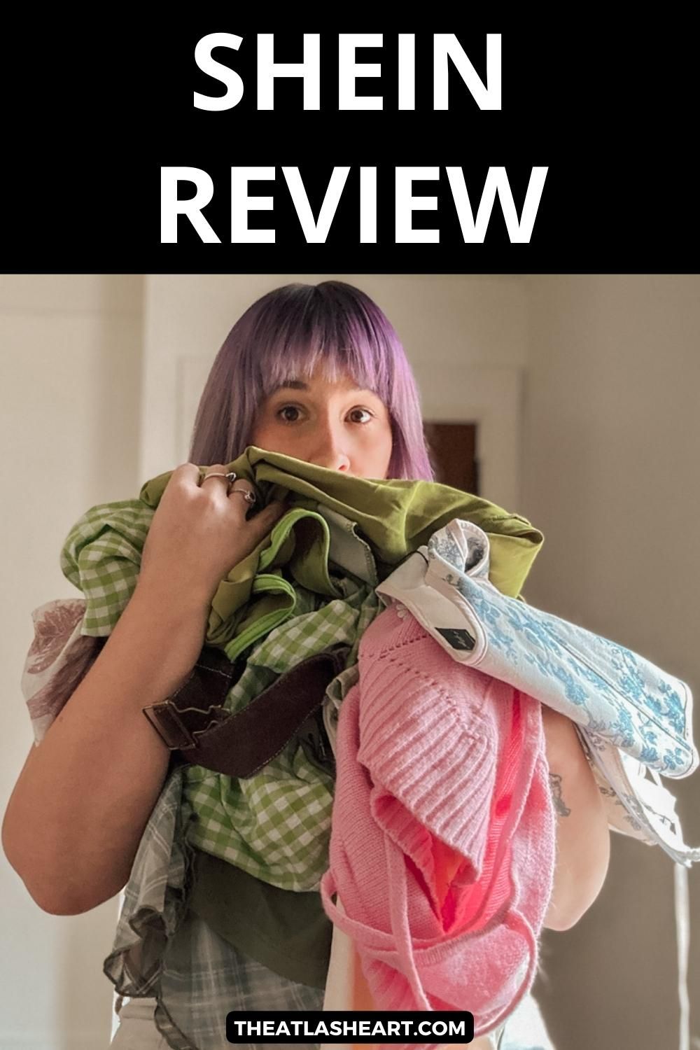 A purple-haired woman holds a pile of multi-colored clothing in a sparse interior space, with the text overlay, "Shein Review."