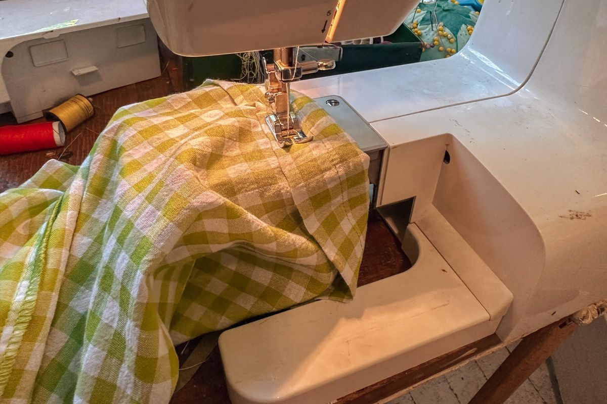 A green and white checkered garment gets hemmed on a white sewing machine.
