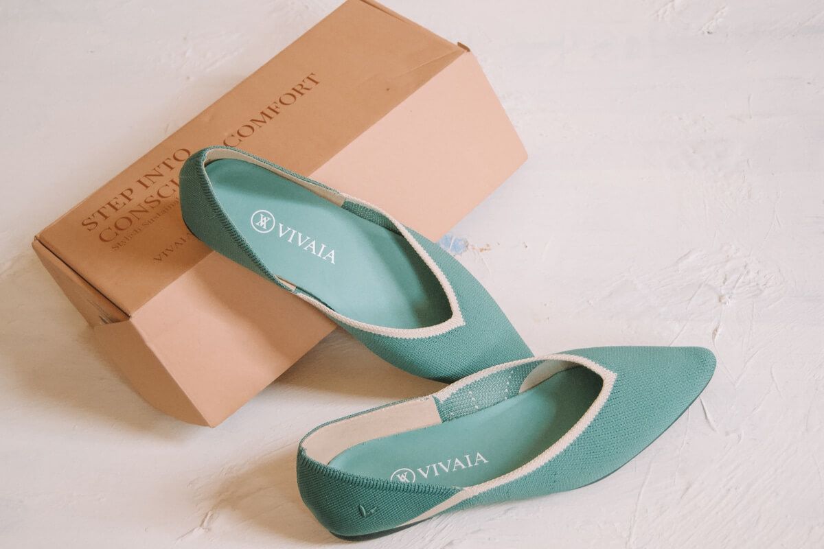 A pair of teal Vivaia flats sitting on their shoebox on a white background.
