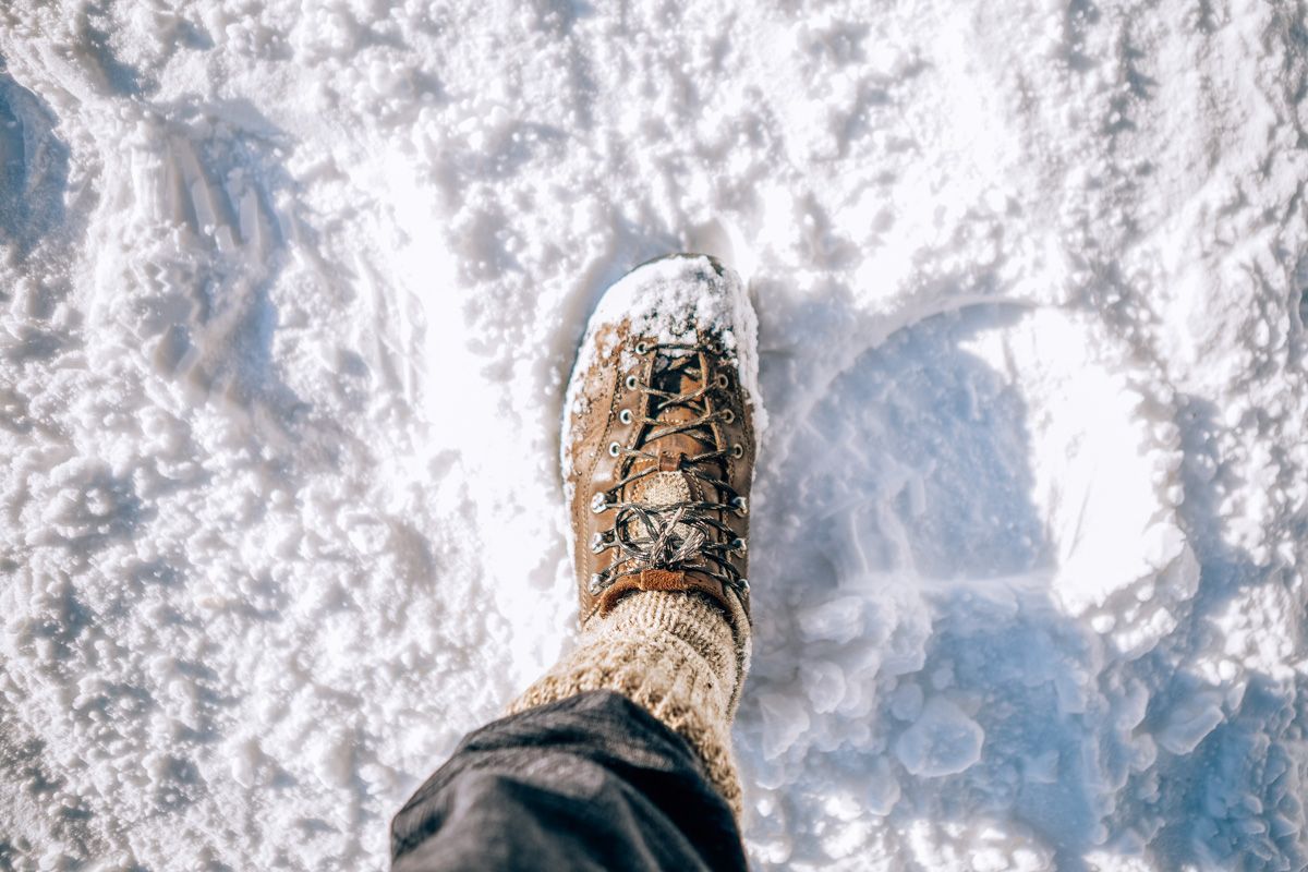 POV-short looking down at a foot in a brown leather boot and thick oatmeal-colored socks, stomping through snow.