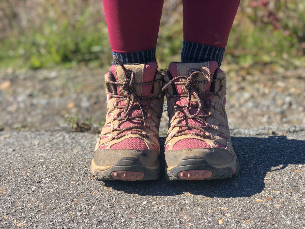 A pair of feet standing on asphalt, hiking socks  with brown, low-top hiking boots and red leggings.