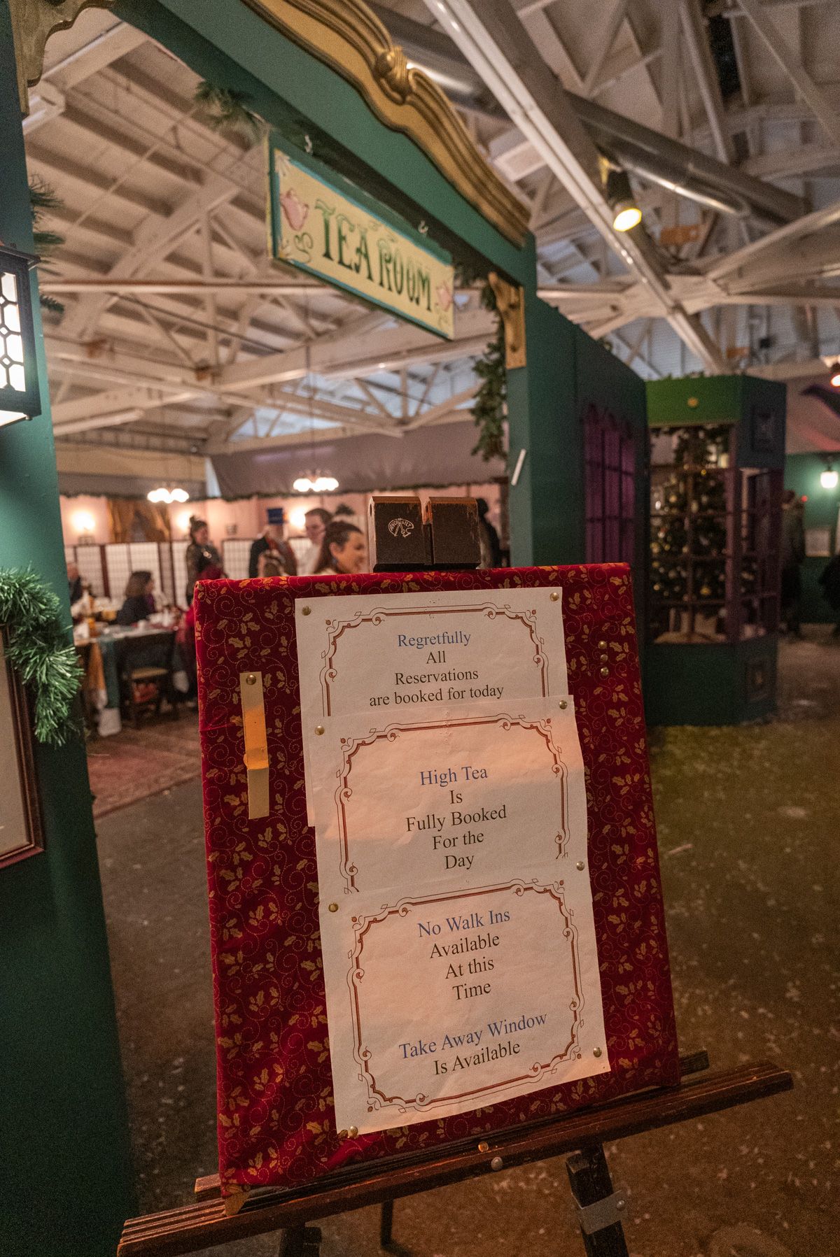 A sign advertising high tea options outside a green booth with a hand-painted sign that reads "Tea Room."