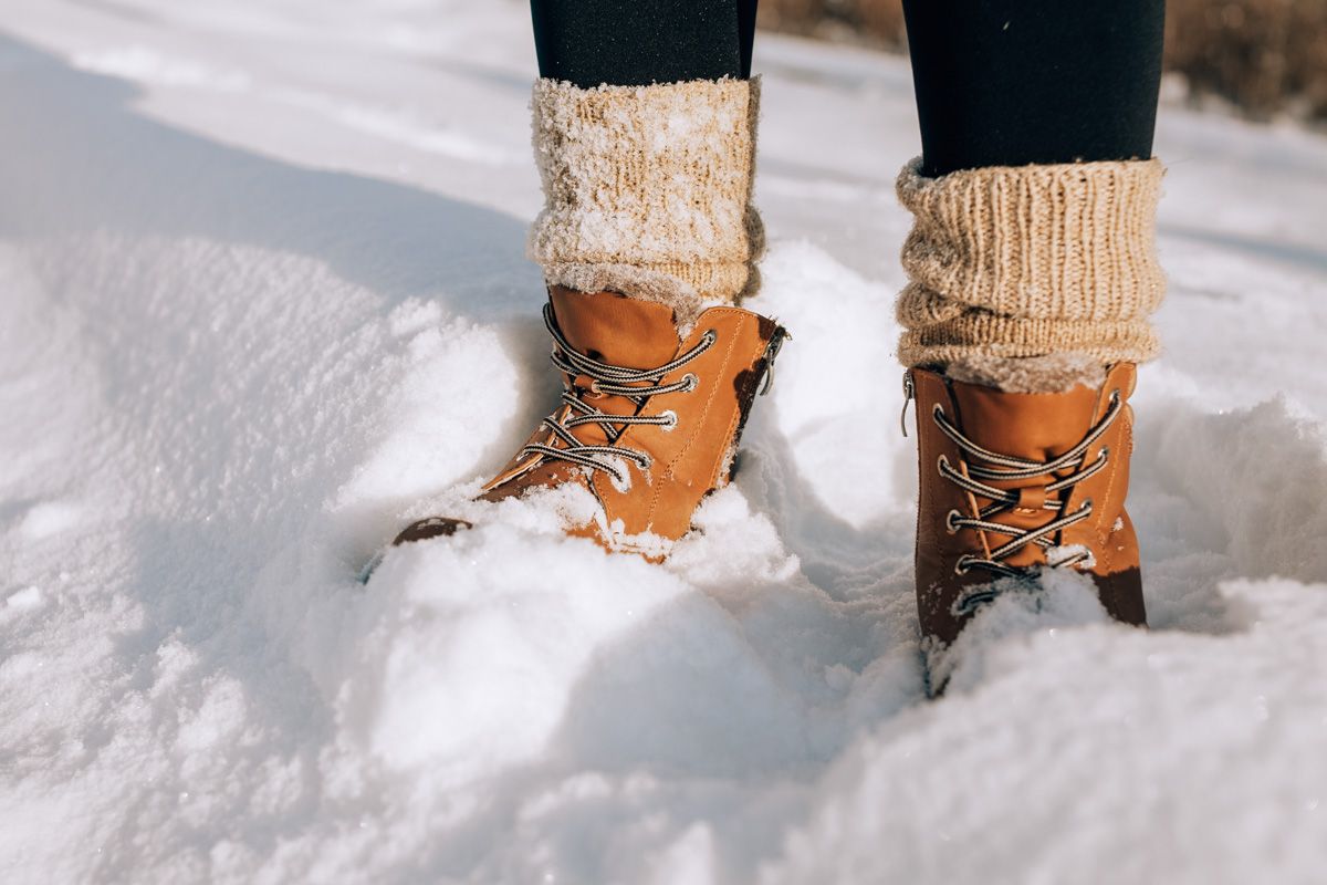 A pair of feet in brown leather boots and thick oatmeal-colored socks, standing in deep snow.
