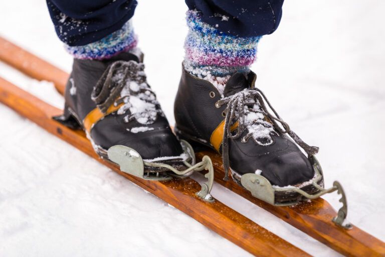 A close-up of a pair of skiier's feet wearing some of the best heated ski socks, balancing on some skis in the snow.