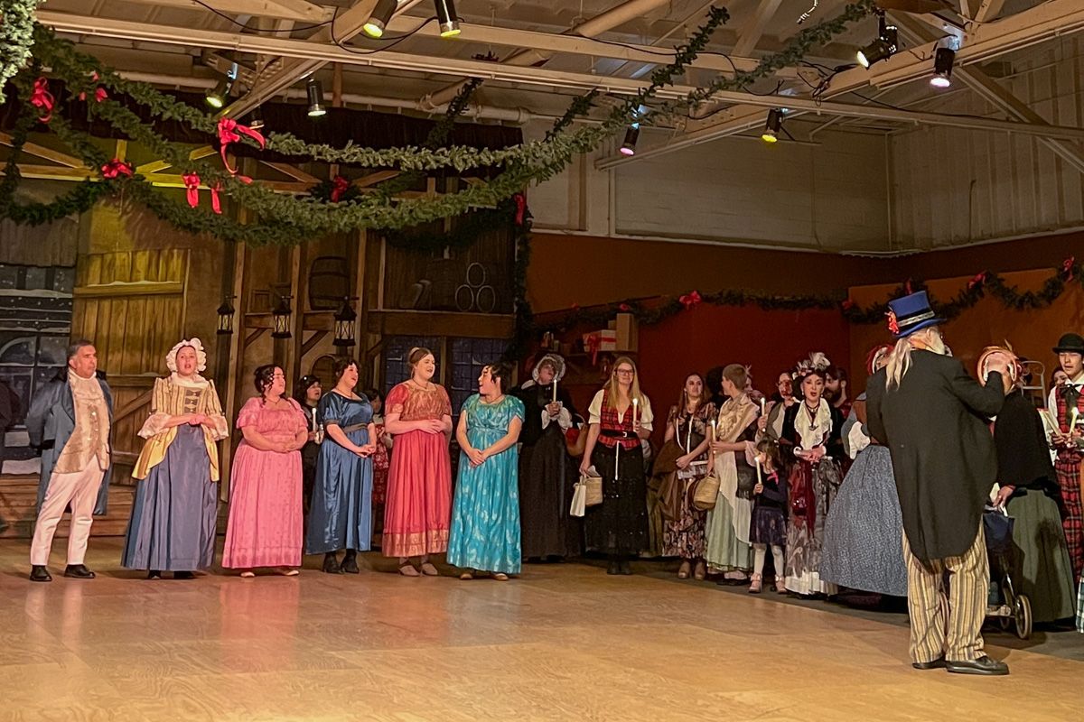 Performers in Dickensian costumes stand lined up a the edge of a dance floor beneath a Christmas garland strung from the rafters above.